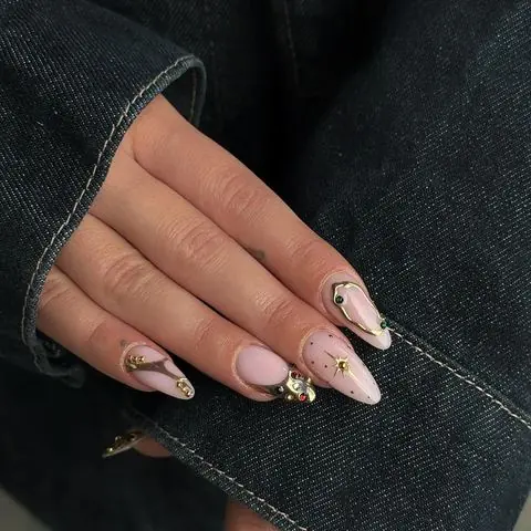 Zartrosa Mandelnägel mit goldenen Chrome-Details und Schmucksteinen