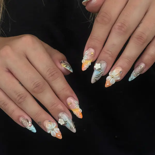 Lange Stiletto-Nägel mit Farbverlauf in Hellblau und Pfirsich, 3D-Blüten und Goldlinien