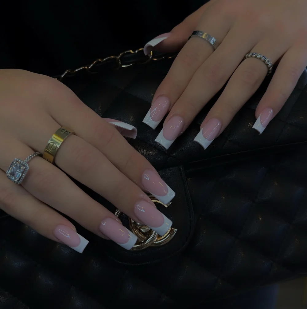 Lange eckige French Nails in Nude und Weiss auf einer schwarzen Steppleder-Handtasche